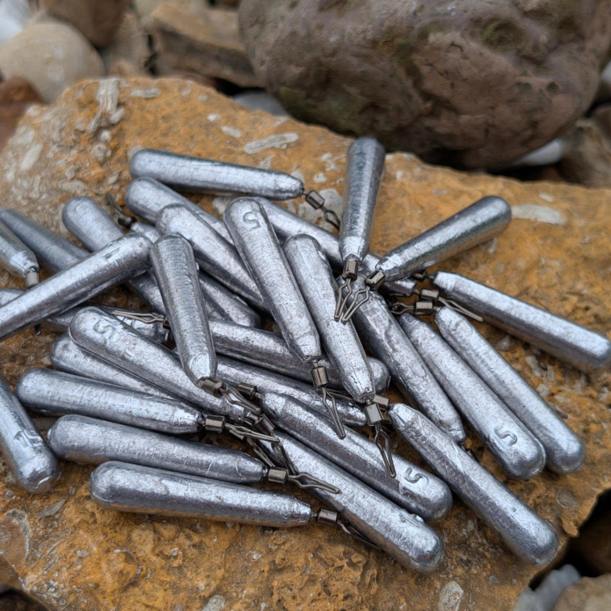 Unpainted cylindrical drop shot weights with line clips displayed on a rock.