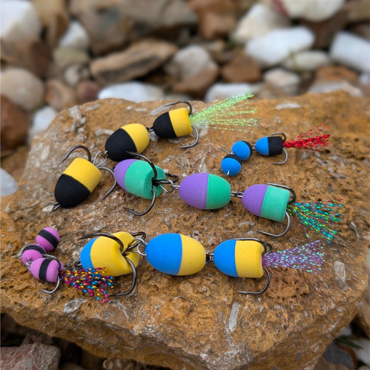 Colorful segmented Mandula fishing lures with treble hooks and flash tails displayed on rocks.