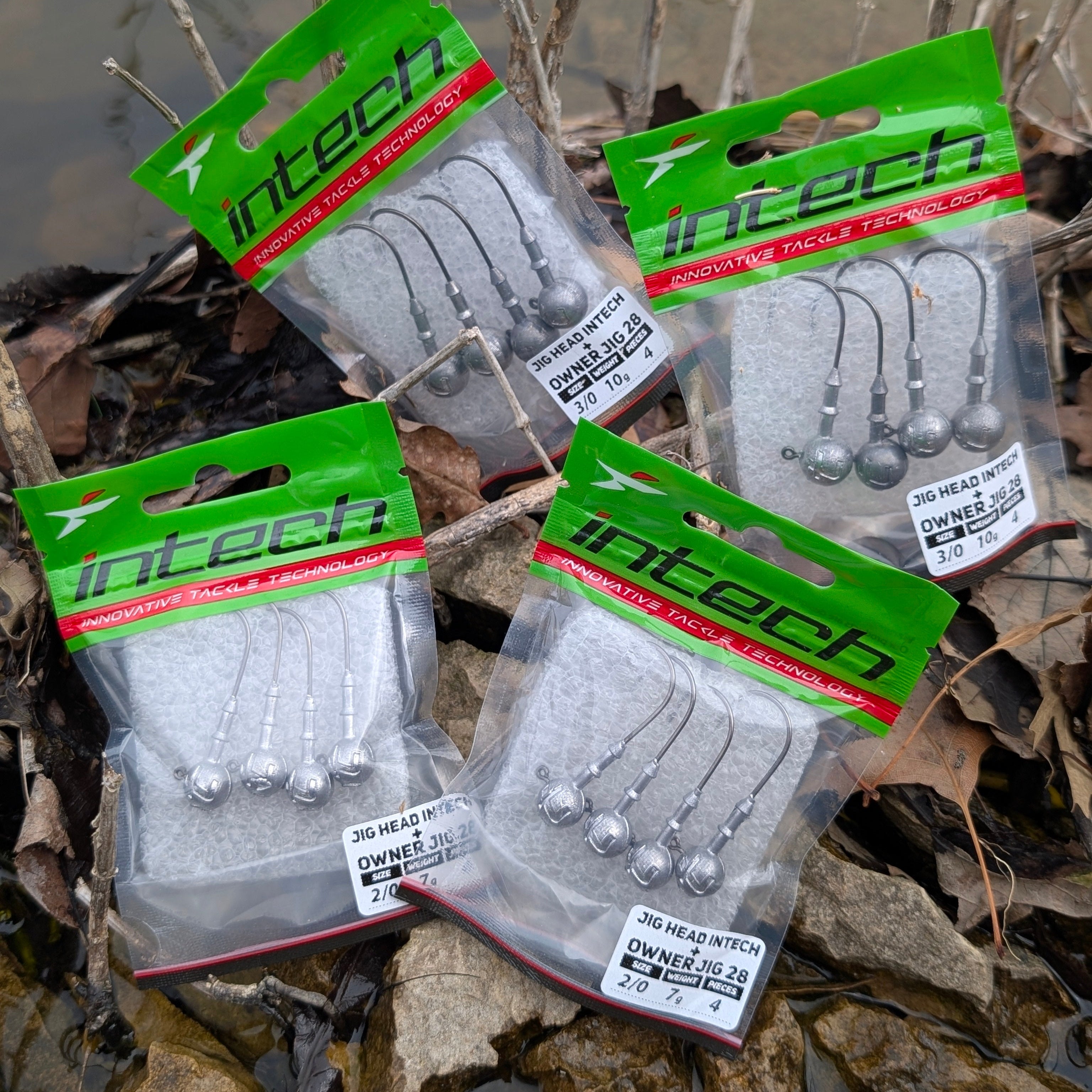 Four packages of Intech fishing hooks on a natural background with water and reeds.